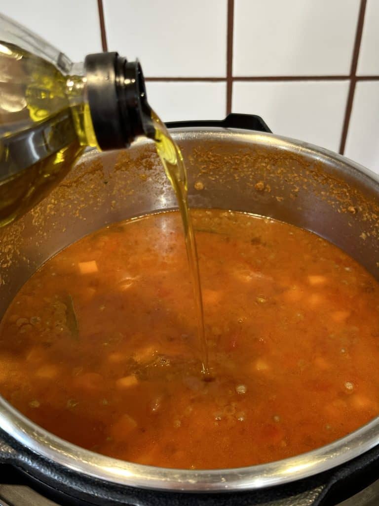 Pouring fresh extra virgin olive oil into a cooked pot of Greek lentil soup