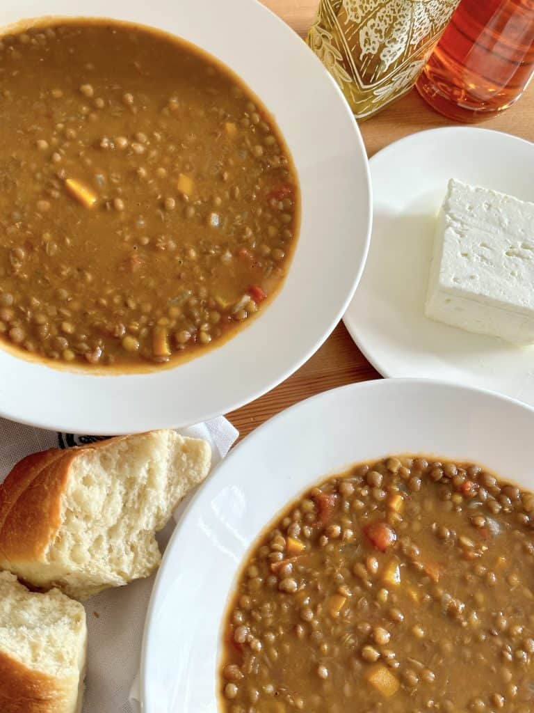 Two bowls of Greek lentil soup served with a piece of bread and a slice of feta