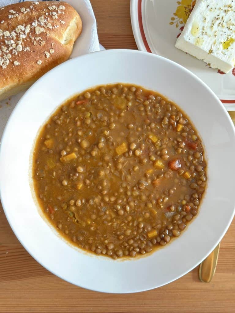 A bowl of Greek lentil soup served with a side of bread and a slice of feta cheese