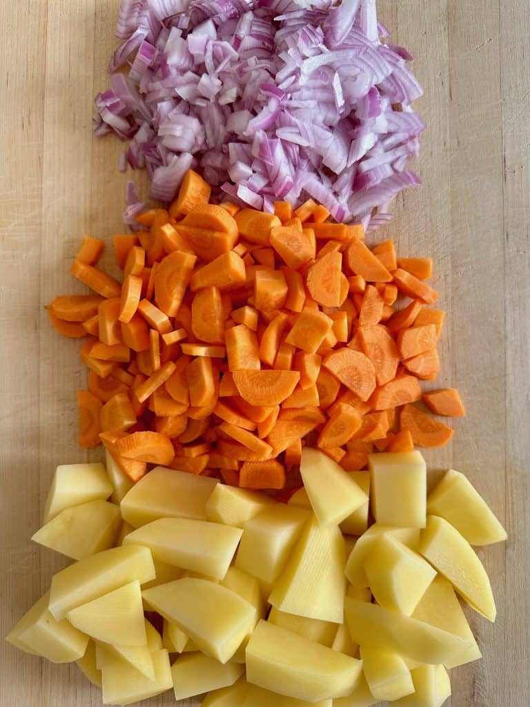 Chopped and peeled potatoes, carrots, and onion on a wooden cutting board