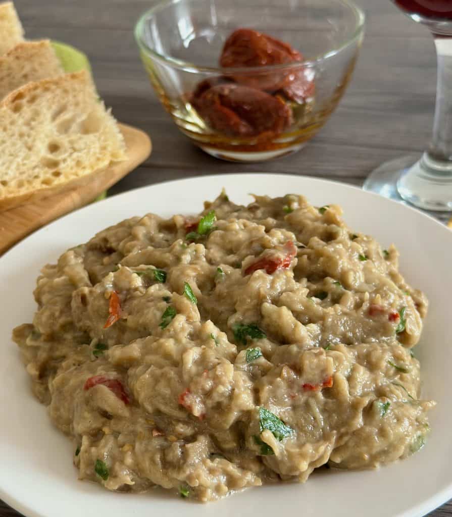 Instant Pot Greek Eggplant Dip on a white plate served with bread and sun-dried tomatoes