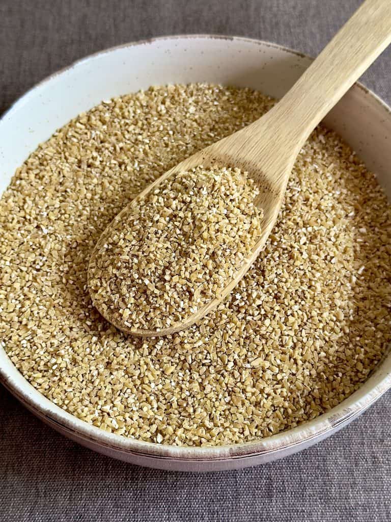 Uncooked bulgur in a bowl with a wooden spoon