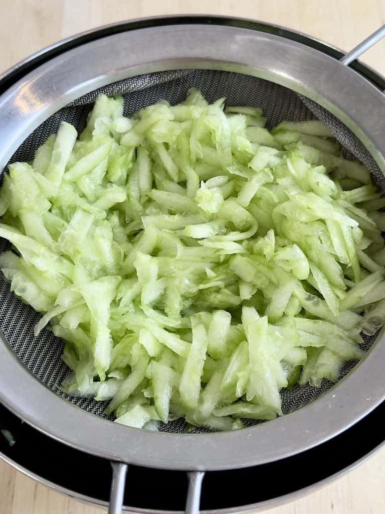 Shredded cucumber in a sieve in a bowl