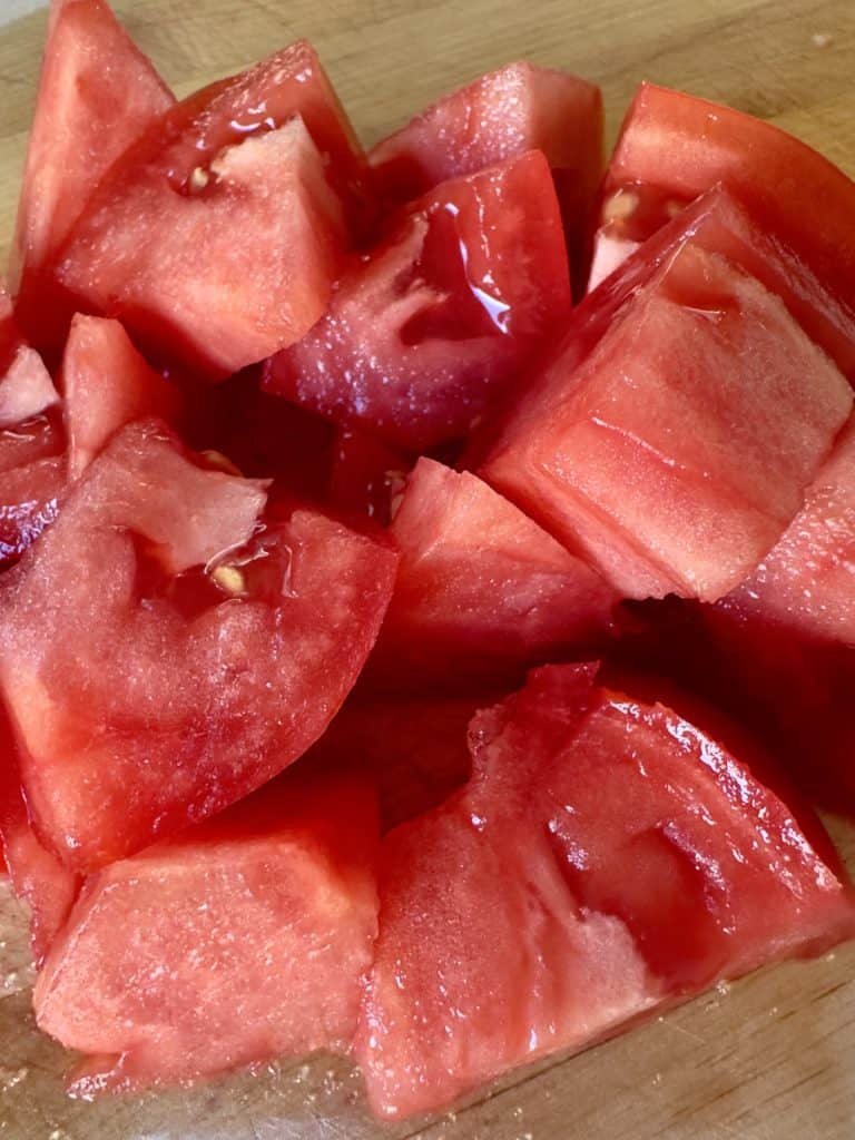 a large tomato cut in pieces on a wooden cutting board