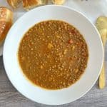 Bowl of Greek lentil soup next to pieces of bread and a golden spoon
