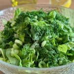 Greek lettuce salad Maroulosalata in a glass bowl next to a lemon and a dish of olive oil